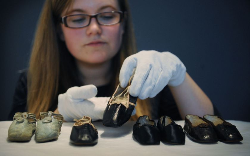 A selection of royal baby shoes are placed on display by a museum staff member
